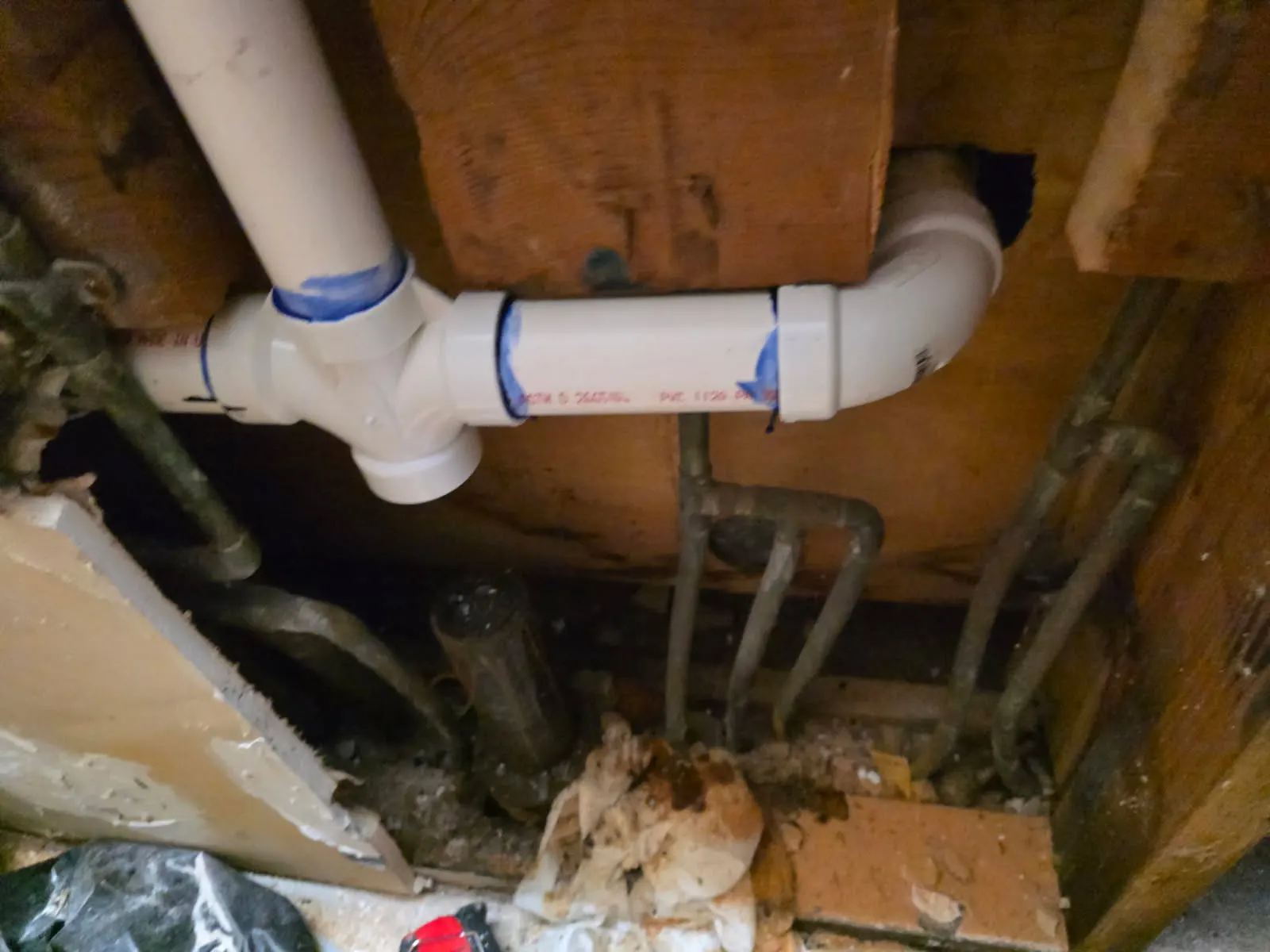 After: new white PVC drain pipes with fresh joints installed in the opened wall to replace the failing cast iron drain line