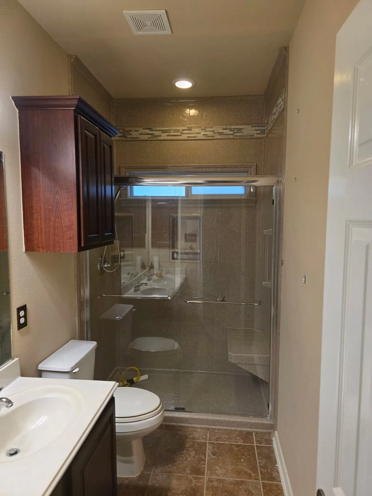 Before photo: dated San Antonio bathroom with dark cherry wall cabinet, framed glass shower, granite-pattern walls and mosaic tile accent band — ready for a full bathroom remodel