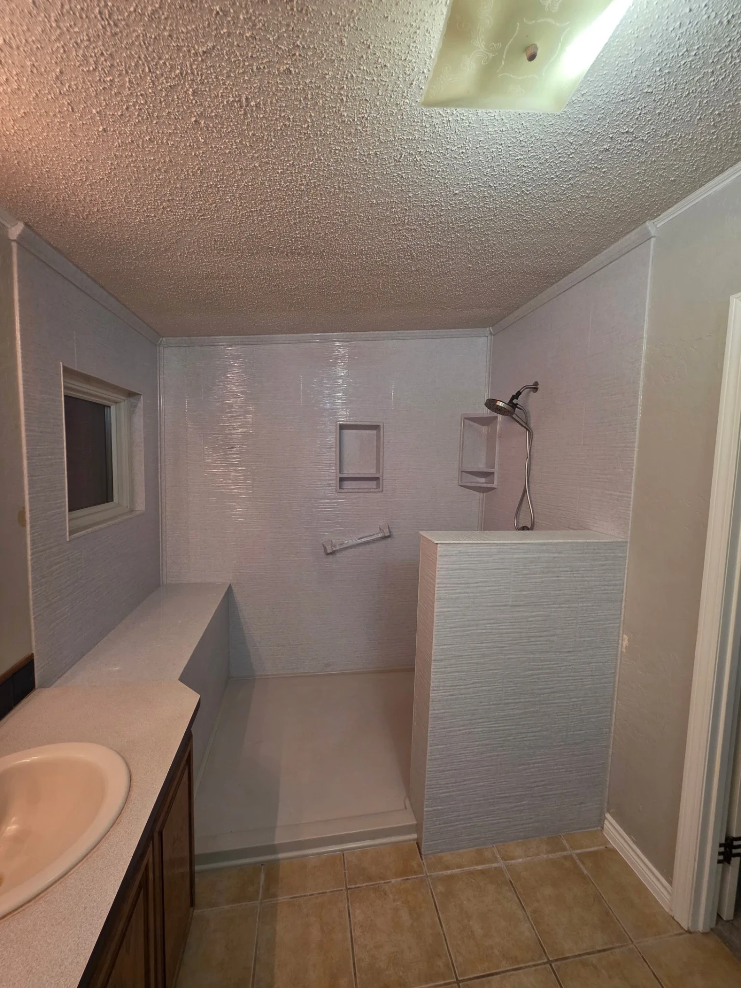 Before photo: dated mobile-home walk-in shower with worn fiberglass walls, popcorn ceiling and original tile floor — ready for a full transformation