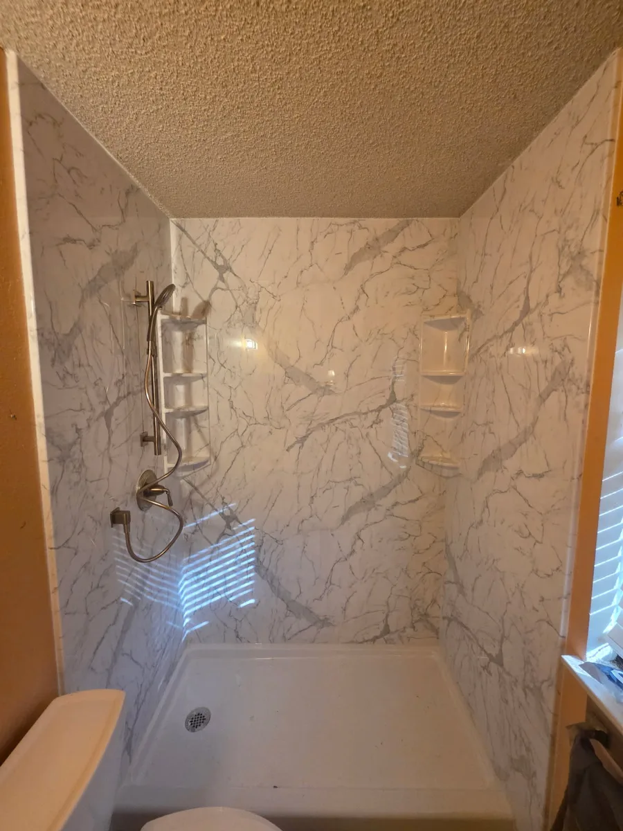 Calcutta marble acrylic shower surround with brushed nickel handheld sprayer, corner shelves and low-profile pan installed in a San Antonio bathroom by Out This World Services