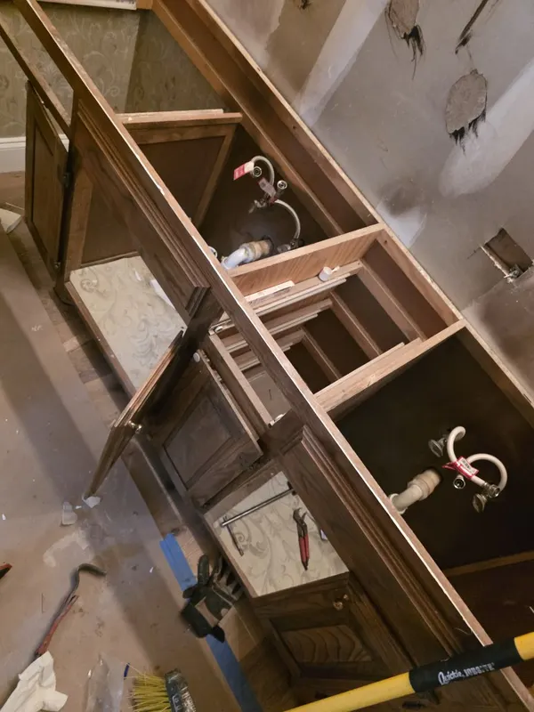 Double-sink vanity mid-demo with cabinet doors off and supply lines exposed — vanity replacement in progress in a San Antonio home