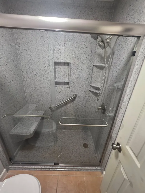 Gray granite-pattern walk-in shower with bypass glass doors, fold-down bench and dual recessed niches