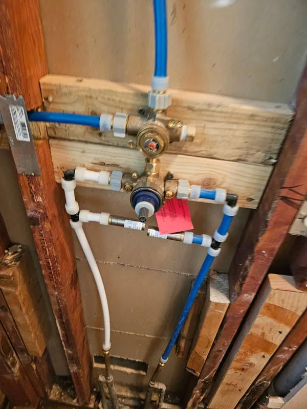 In-progress shower valve rough-in with new PEX supply lines, brass mixing valve and tub spout drop — open-wall plumbing work by Out This World Services