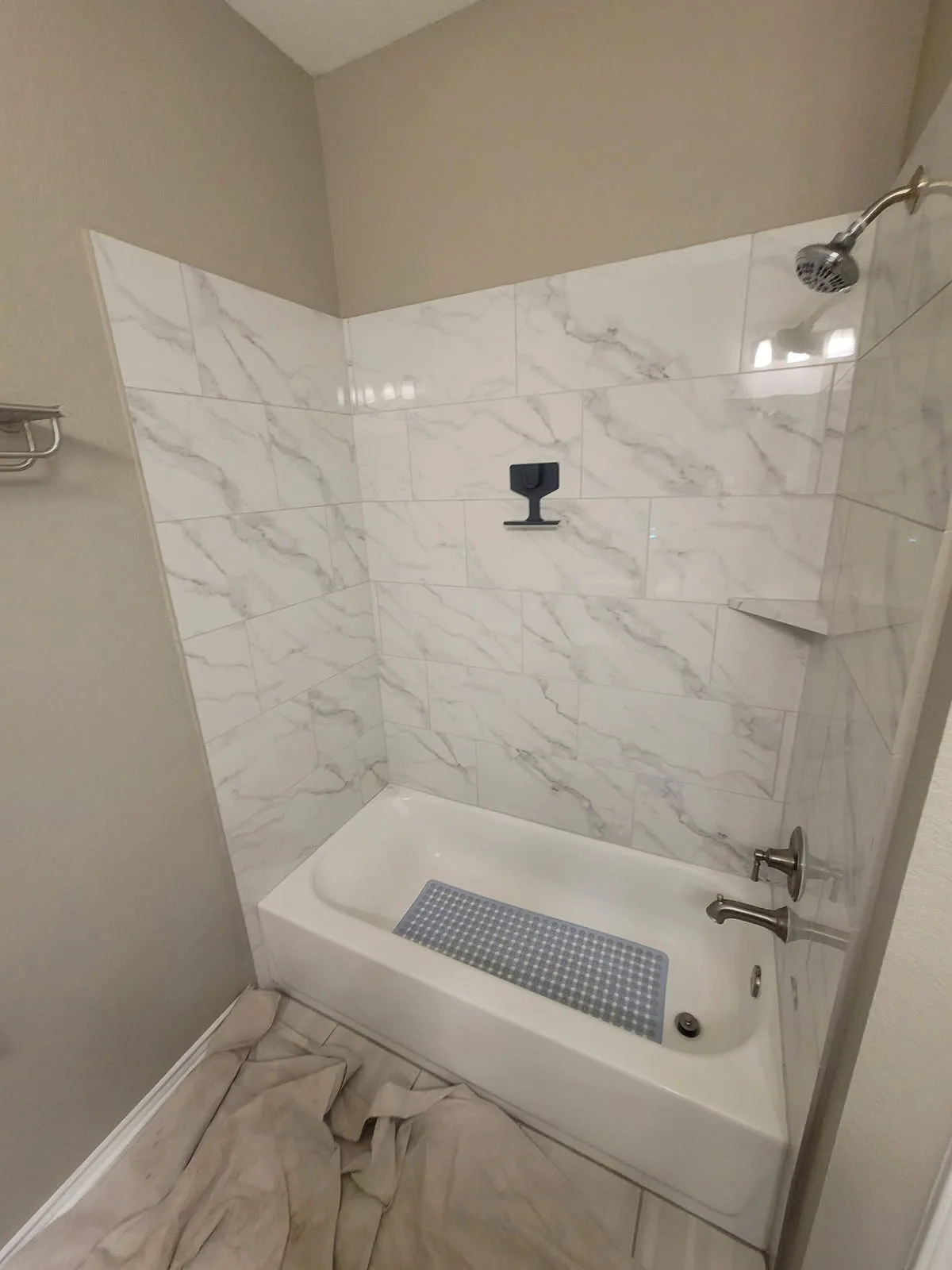 Tub-and-shower combo with marble-pattern tile walls, brushed-nickel showerhead and tub spout, and built-in corner shelf — clean San Antonio bathroom remodel