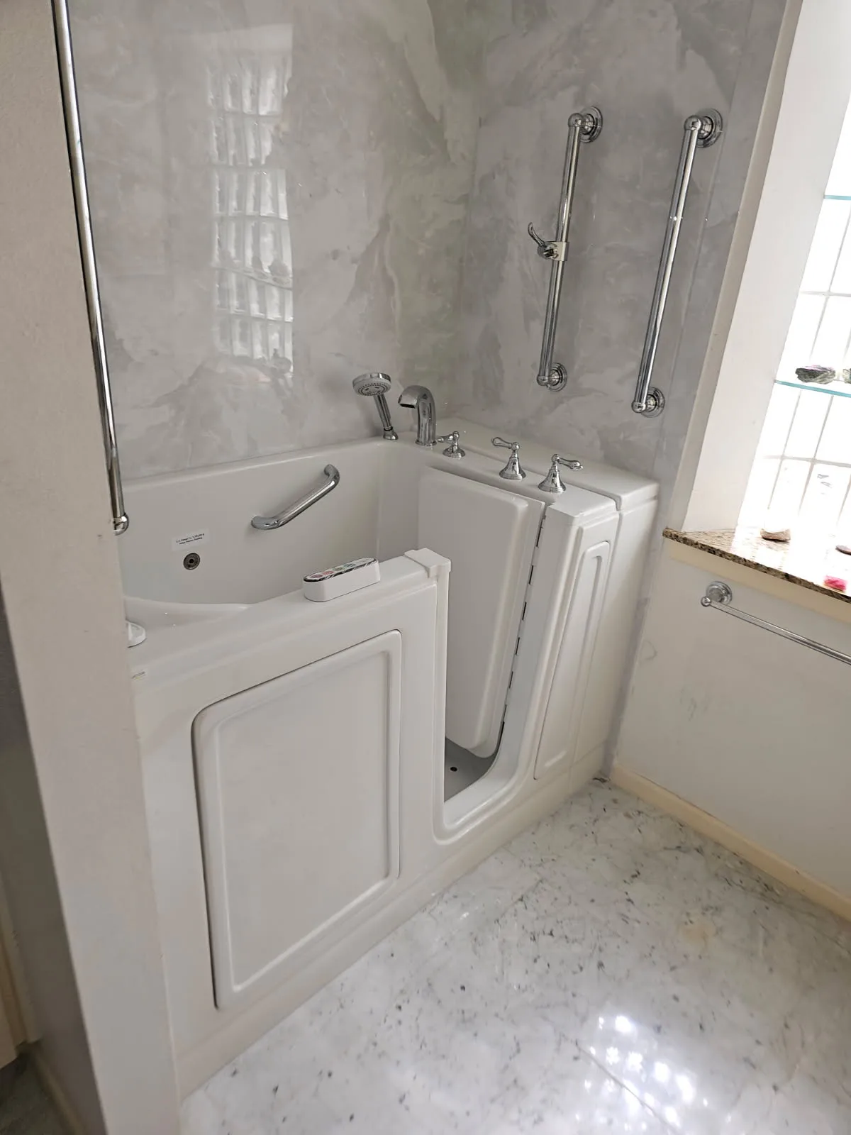 White walk-in tub with inward-swing door, chrome handheld shower and dual full-length chrome grab bars against a marble-pattern surround — accessible bathing install in San Antonio