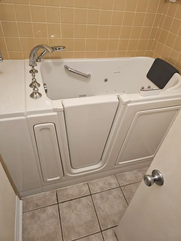 Walk-in tub with inward-swing door, hydrotherapy jets, chrome handheld faucet and safety grab bar installed for accessible bathing in a San Antonio home