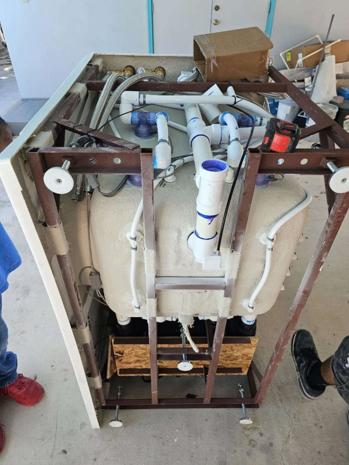 Walk-in tub tipped up on its steel frame in the shop, exposing the underside plumbing, pump lines and adjustable feet during a full inspection and repair by Out This World Services