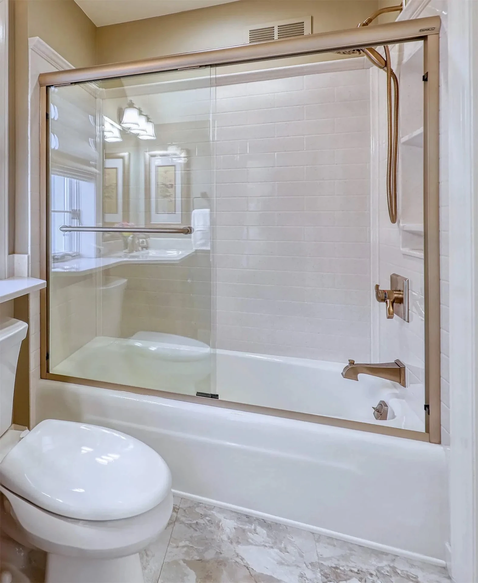 Classic white tub-and-shower combo with subway-tile walls, frameless sliding glass door and matching champagne-bronze fixtures