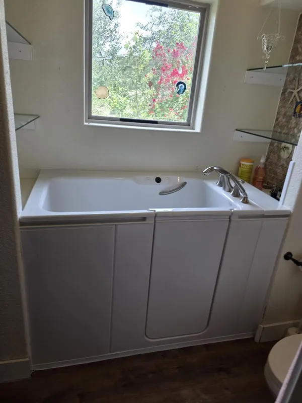 White step-in walk-in tub with brushed-nickel widespread faucet and garden-view window — accessible bathing install in a San Antonio bathroom